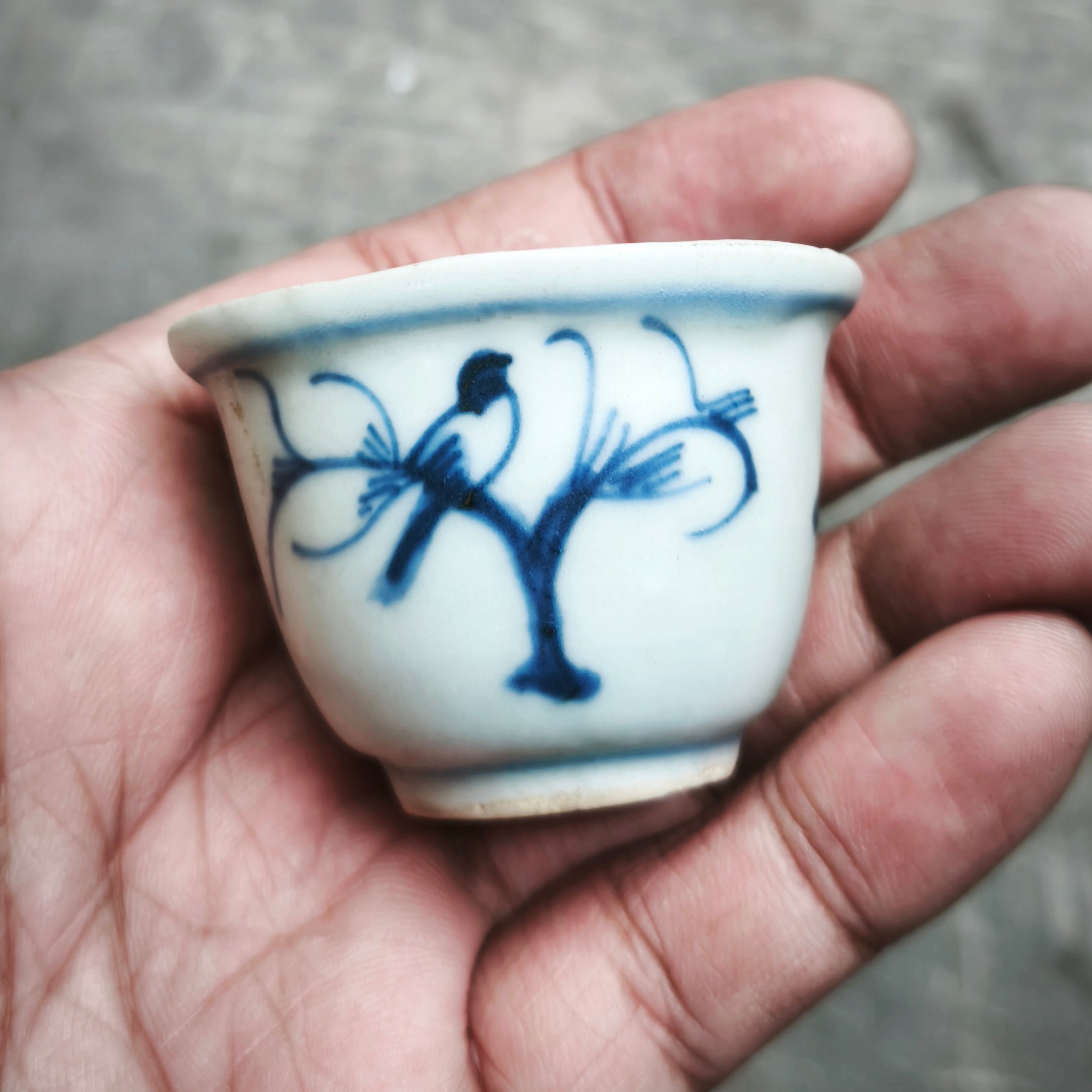 Small white ceramic cup with blue floral design held in a hand against a neutral background