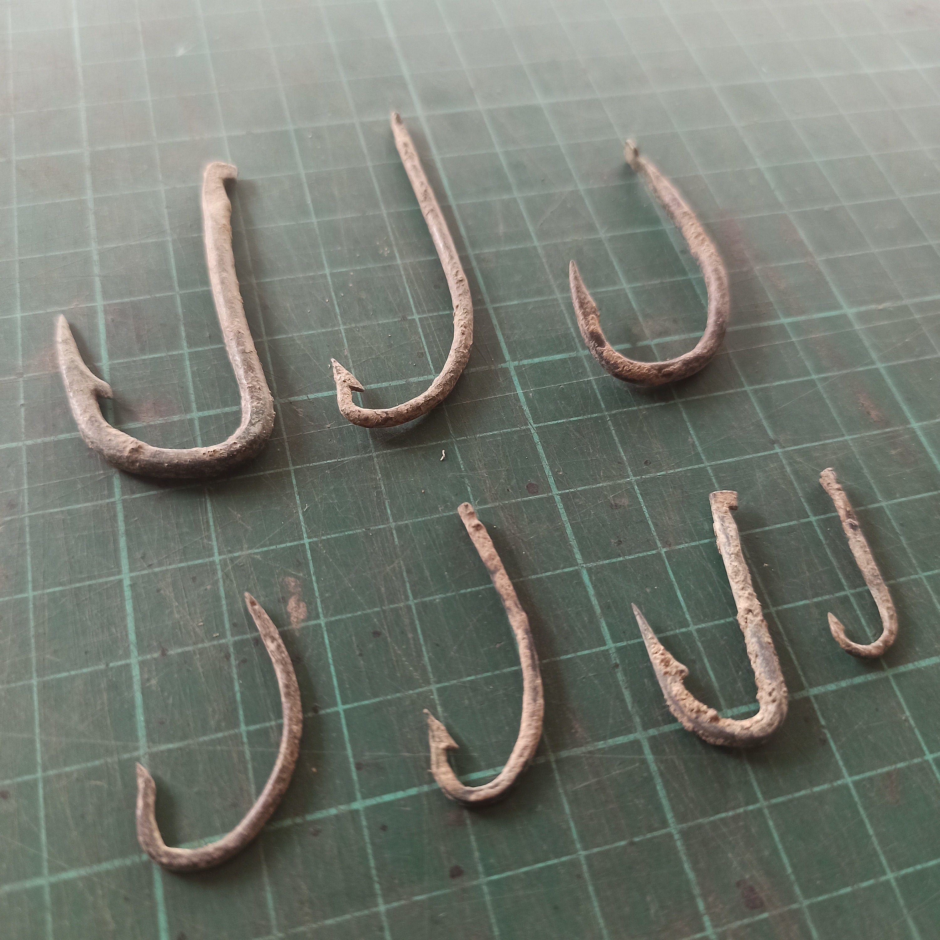 Set of rusty fishing hooks on a green cutting mat with grid lines